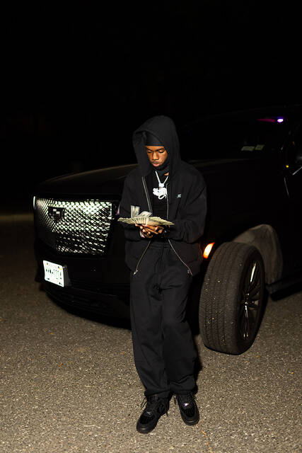 RodSlime counting cash in front of a black SUV at night.