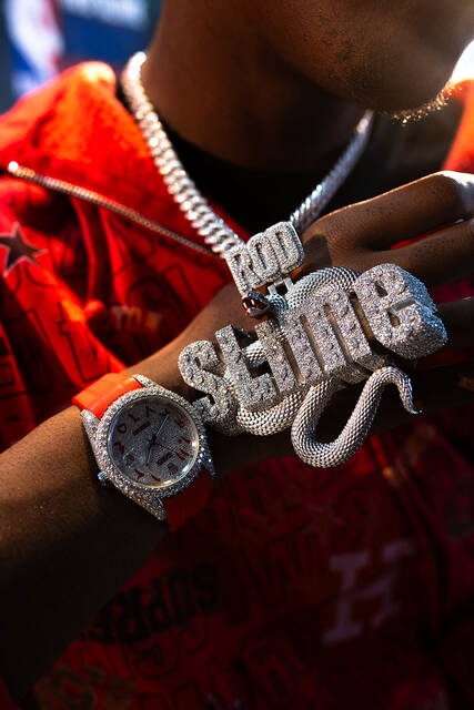 Close-up of an iced Slime pendant and chain over a red jacket.